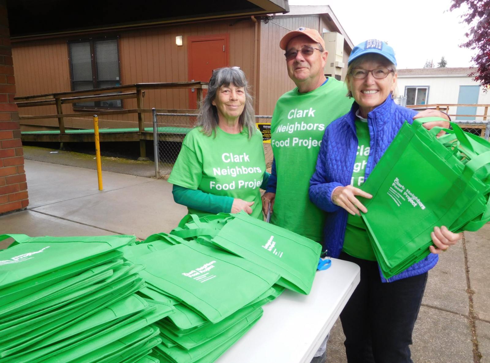 Neighborhood Food Project volunteers stand with stacks of green bags used by food donors to collect nonperishable food for upcoming Collection Days.