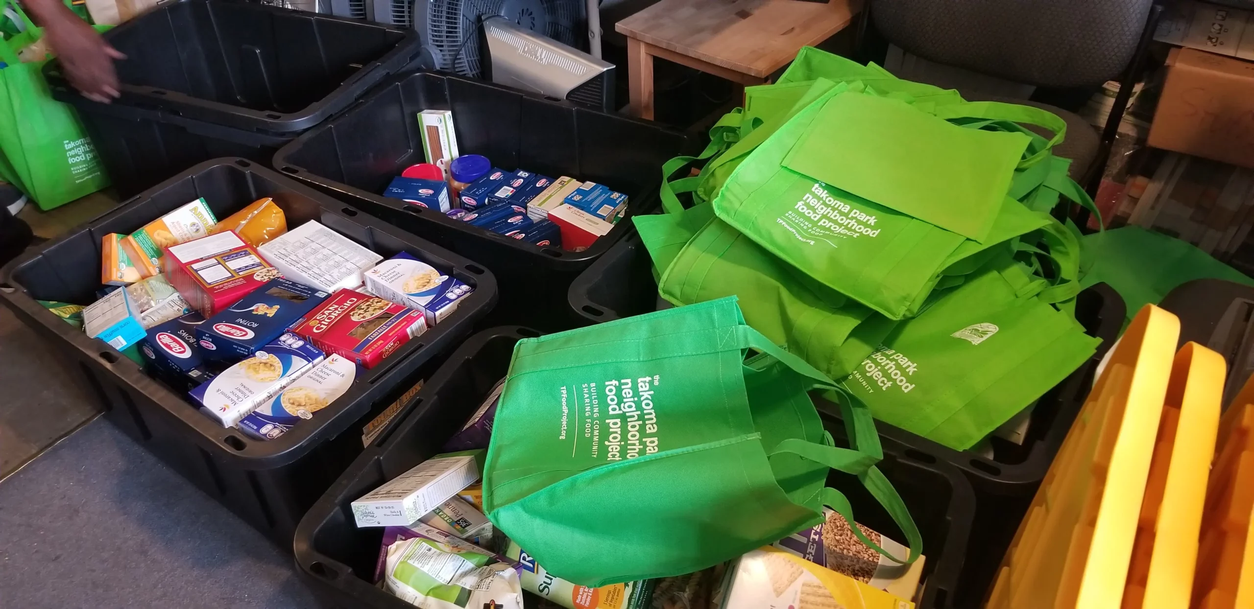 Green food donation bags and nonperishable groceries are arranged in bins as volunteers prepare donations for partner pantries.