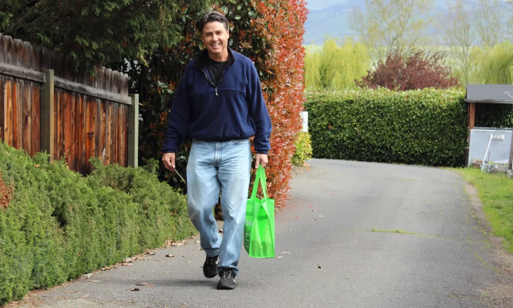 A volunteer carries a green Neighborhood Food Project bag from his home to be collected for an upcoming Collection Day.