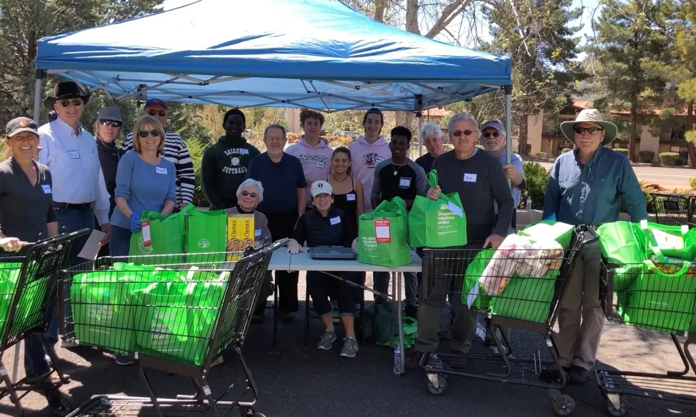 Volunteers stand under a tent with carts and green bags filled with donated nonperishable food during a Neighborhood Food Project Collection Day.